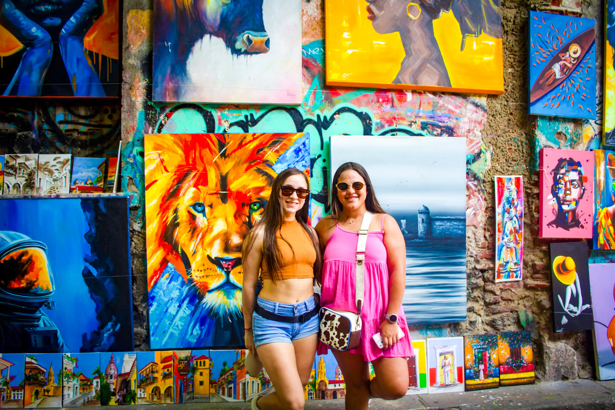 Tourists in front of colorful street art in Cartagena's Walled Old City, featuring vibrant paintings.