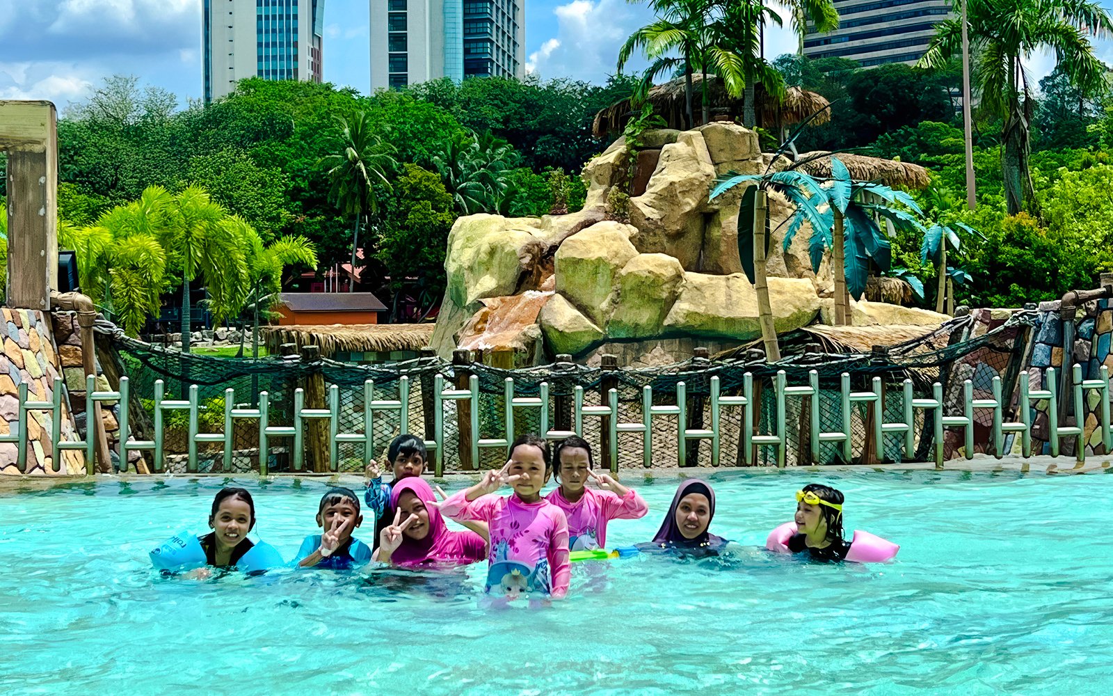Family enjoying the pool at Wet World Water Park Shah Alam with slides and palm trees in the background.
