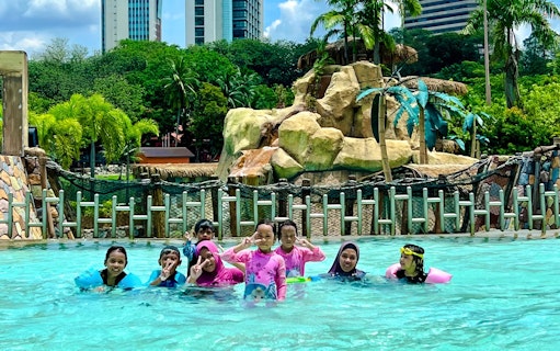 Family enjoying the pool at Wet World Water Park Shah Alam with slides and palm trees in the background.