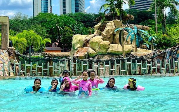 Family enjoying the pool at Wet World Water Park Shah Alam with slides and palm trees in the background.