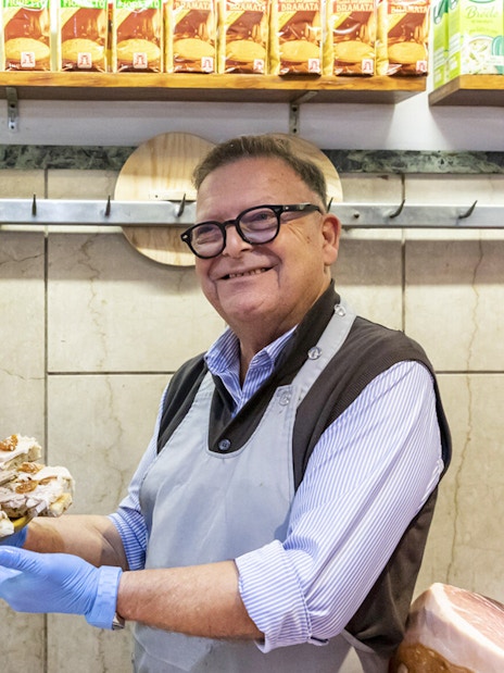 Man in Trastevere shop holding a platter of porchetta slices, Rome.