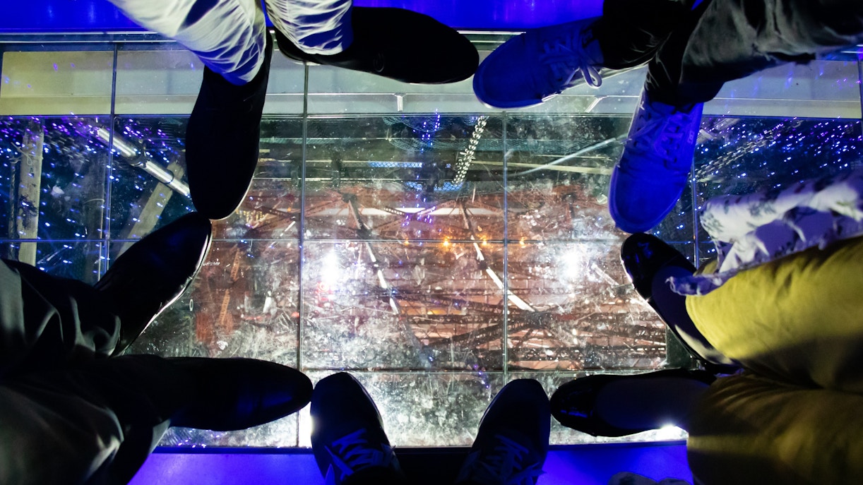 Visitors standing on the glass floor at Tokyo Tower, viewing the illuminated structure below.