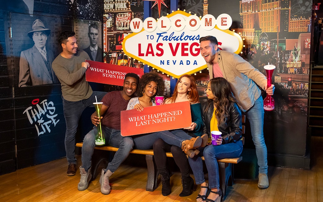 Group of friends posing with signs at the Welcome to Las Vegas sign, enjoying Go City: Las Vegas Explorer.