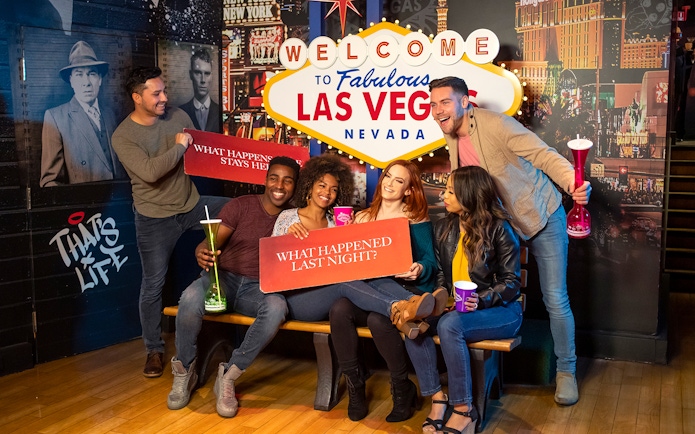 Group of friends posing with signs at the Welcome to Las Vegas sign, enjoying Go City: Las Vegas Explorer.