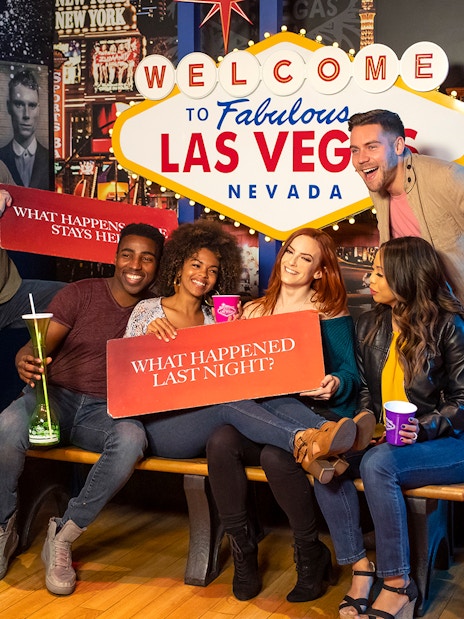 Group of friends posing with signs at the Welcome to Las Vegas sign, enjoying Go City: Las Vegas Explorer.