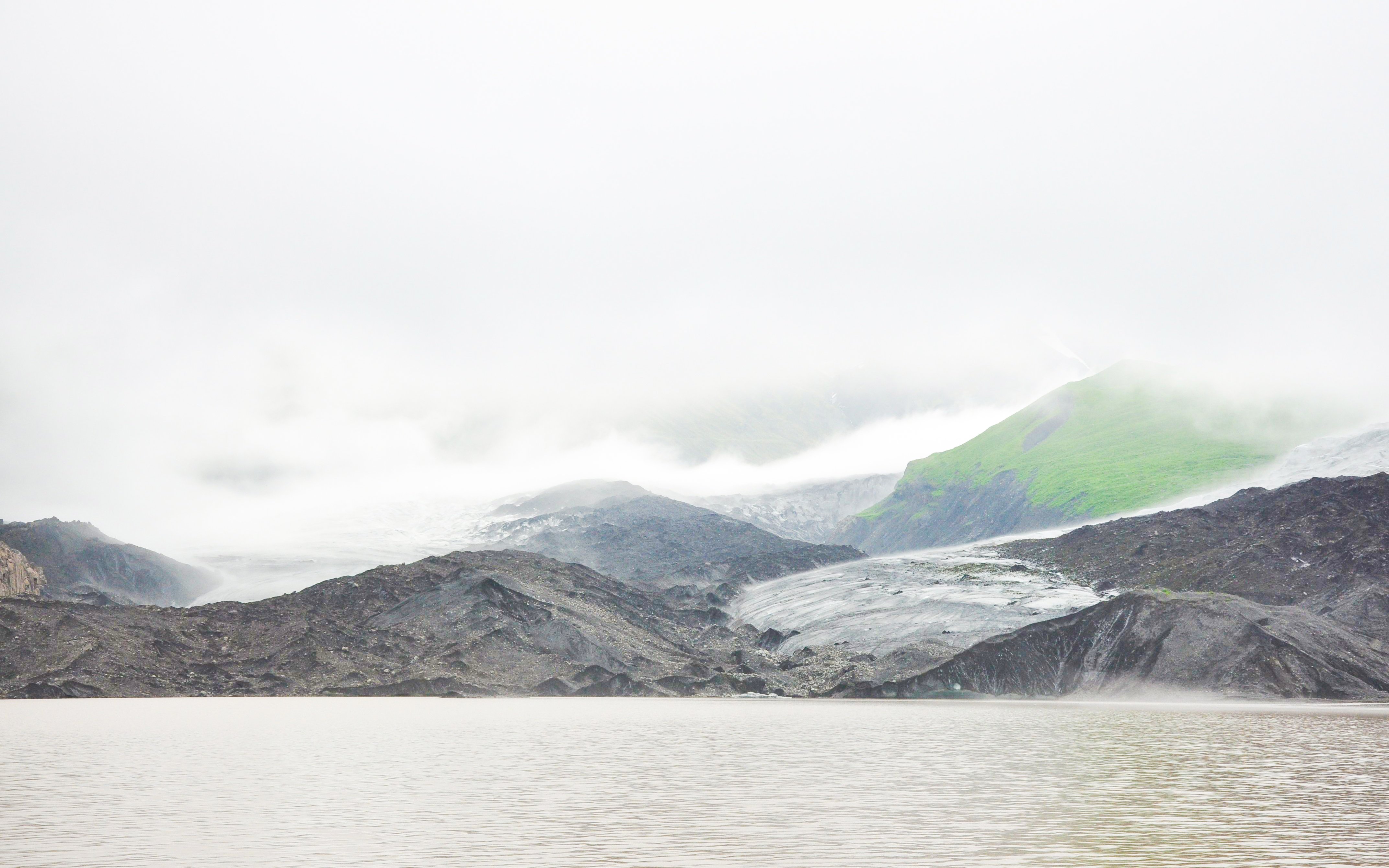 Falljokull glacier shrouded in fog with rocky terrain and green hills, Iceland.