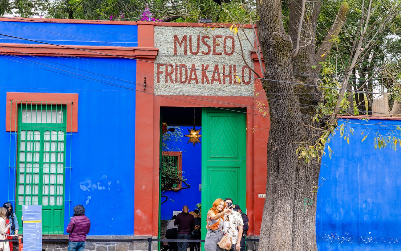 Visitors exploring the vibrant courtyard of the Frida Kahlo Museum in Mexico City.