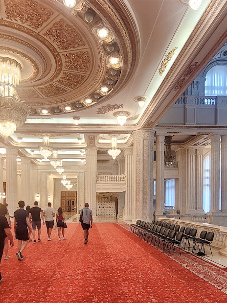 Visitors walking through ornate hall in Palace of Parliament Bucharest.