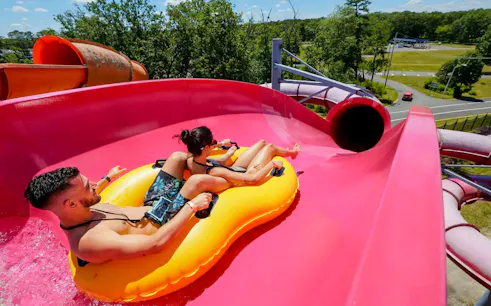 Two people on a yellow raft sliding down a pink water slide at Hurricane Harbor New Jersey.