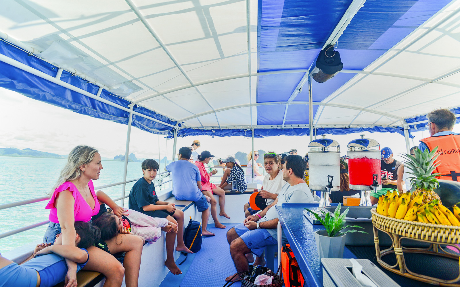 Tourists relaxing on a boat tour at Phang Nga Bay with refreshments and tropical scenery.