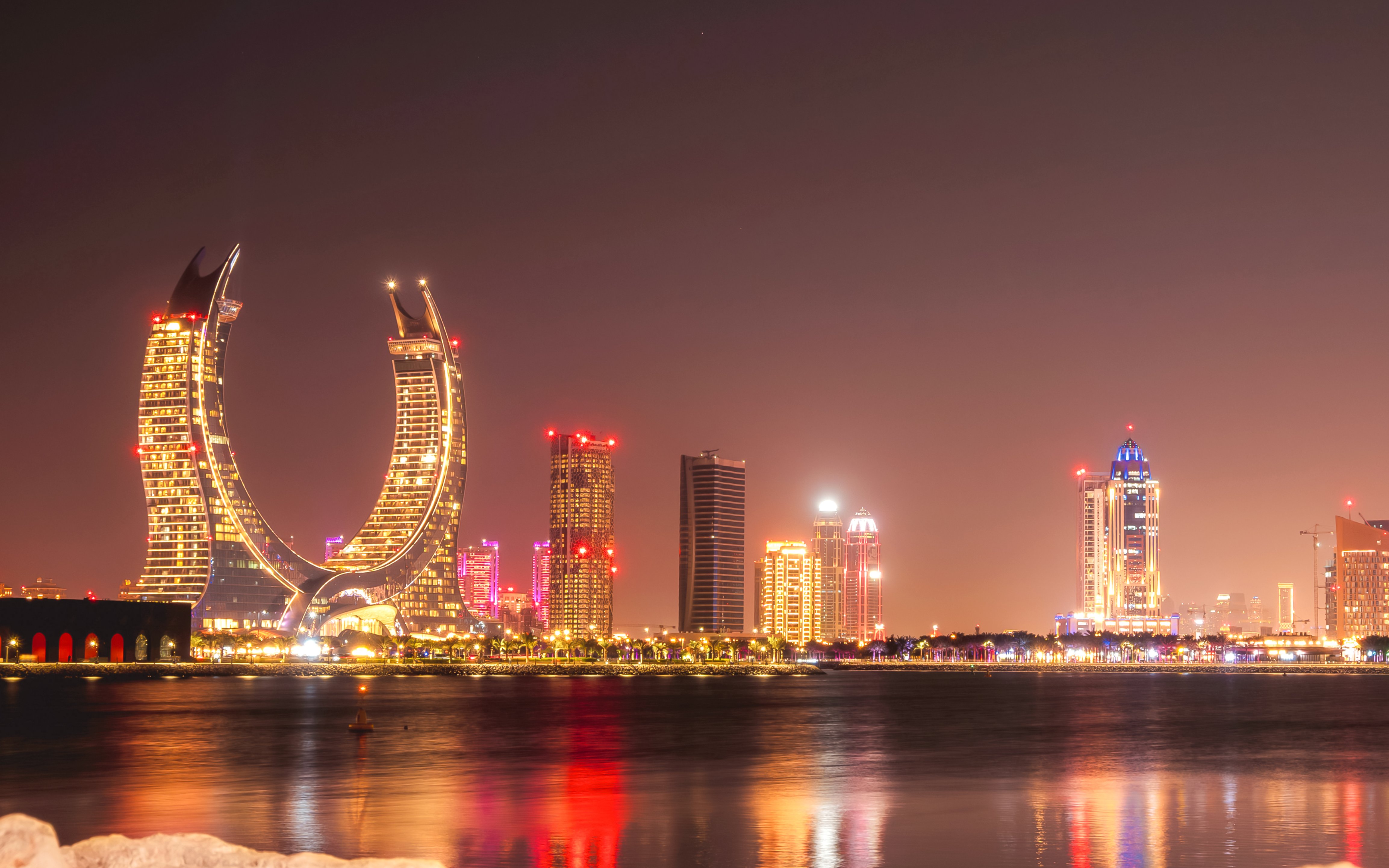 Illuminated skyscrapers by the sea at night in Doha, Qatar.