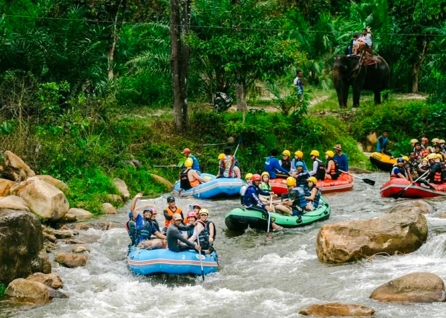 Group rafting on a river in Krabi with lush jungle and elephant in the background.