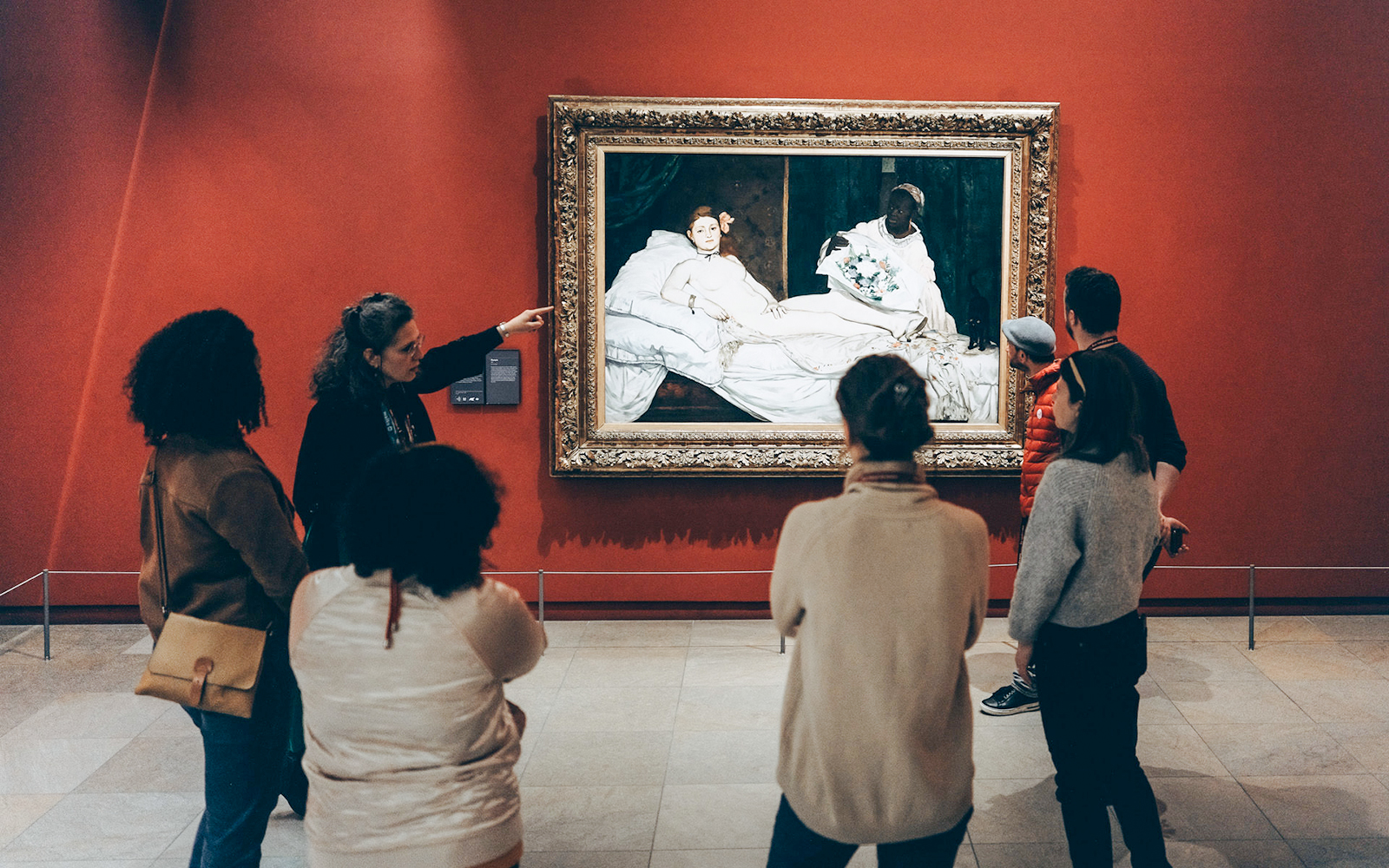Tour guide with tourists viewing a painting inside Orsay Museum, Paris.