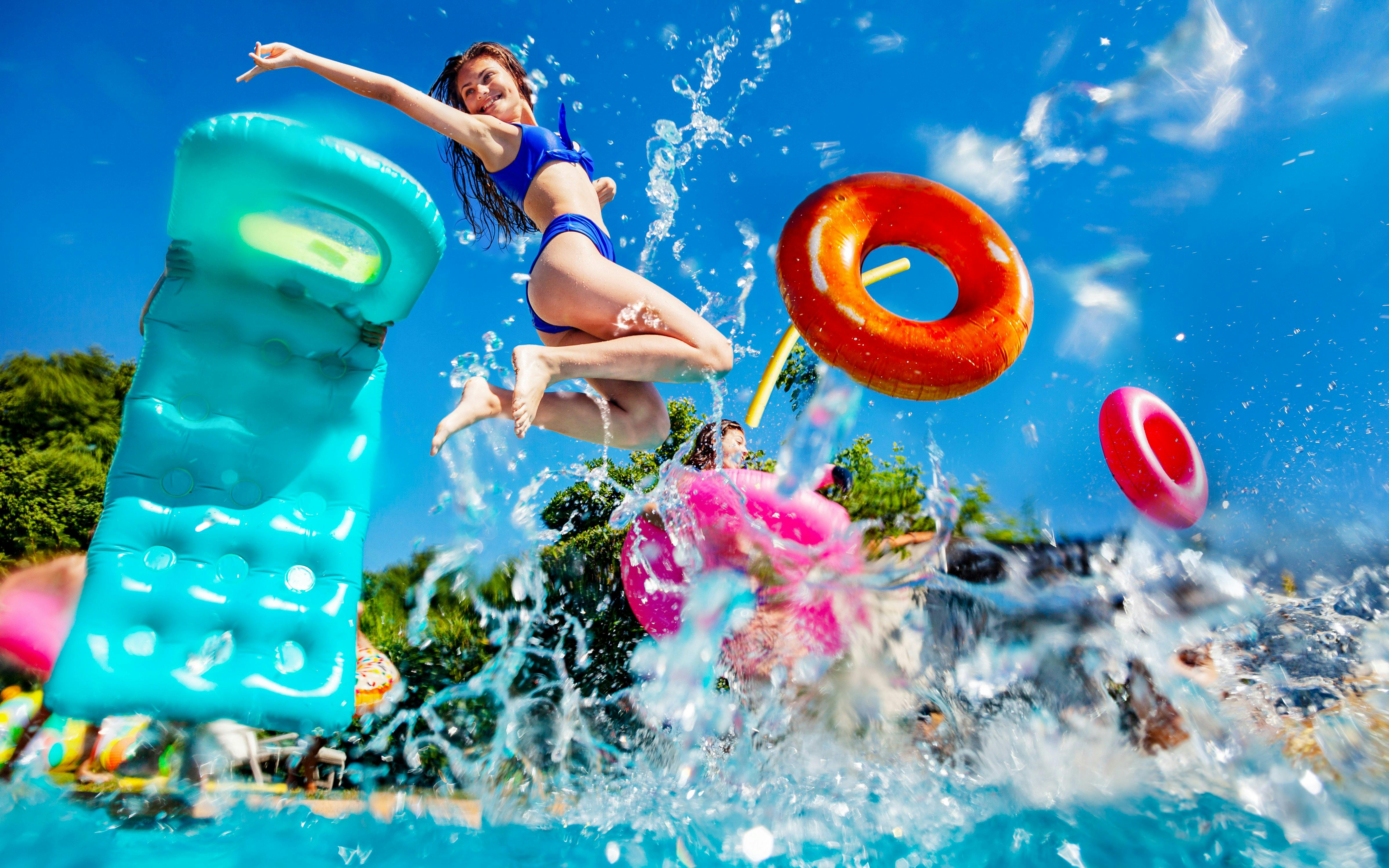 Person jumping into a pool with colorful inflatables at a lively pool party.