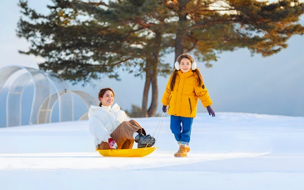 Child pulling sled with adult at Vivaldi Park Snowy Land, Seoul day tour.