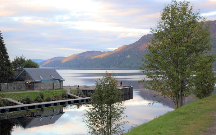 Fort Augustus view of Loch Ness with a small building and mountains in the background.