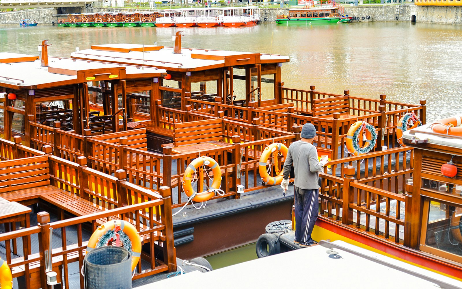 Sightseeing boat docked at Clarke Quay, Singapore River, with a person preparing for a tour.