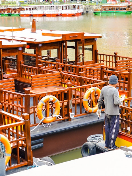 Sightseeing boat docked at Clarke Quay, Singapore River, with a person preparing for a tour.