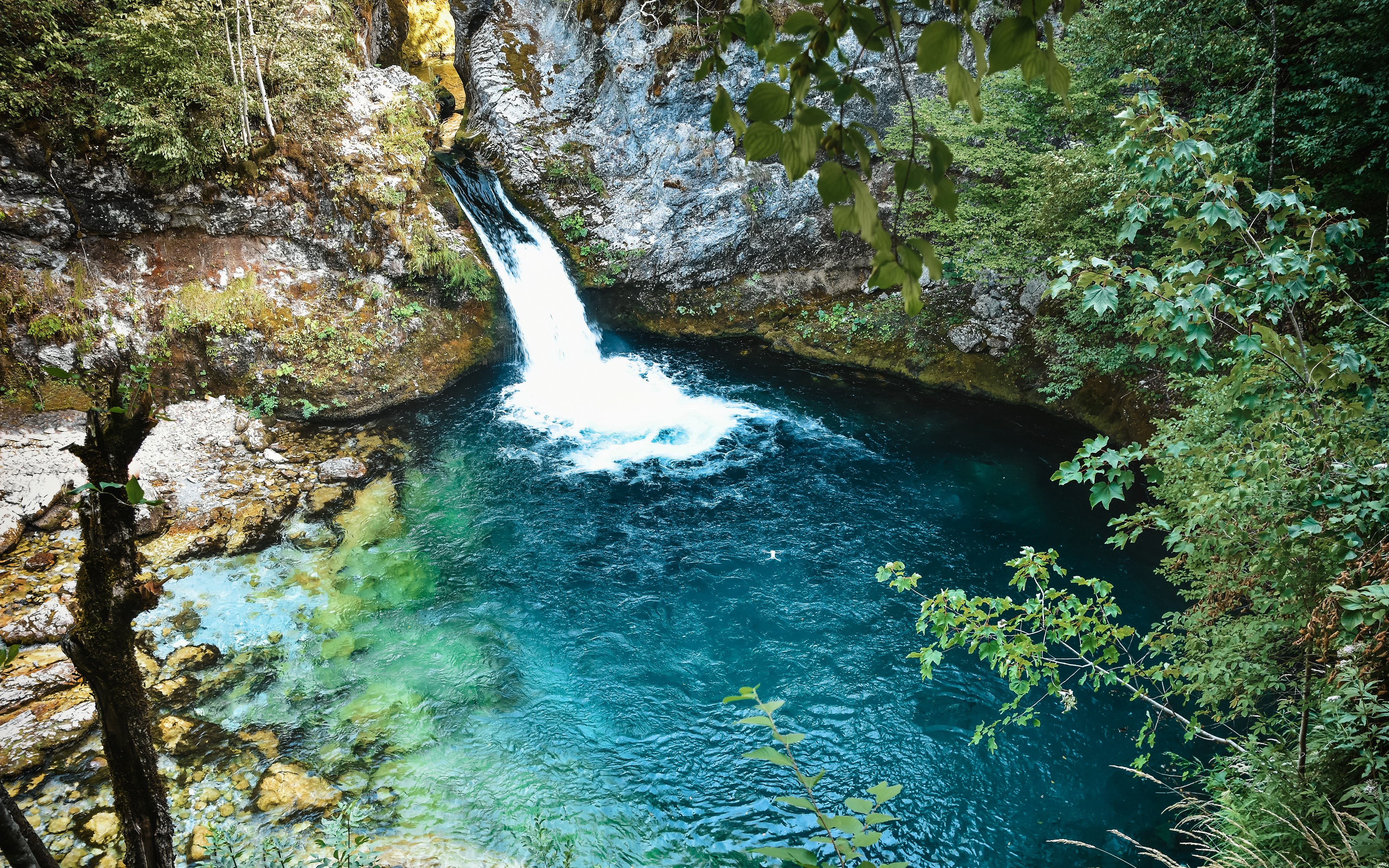 Waterfall flowing into the Blue Eye spring surrounded by lush greenery in Theth, Albania.