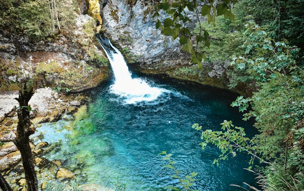 Waterfall flowing into the Blue Eye spring surrounded by lush greenery in Theth, Albania.