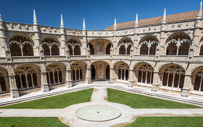 Cloister of Jerónimos Monastery in Lisbon, Portugal, featuring ornate arches and manicured lawns.