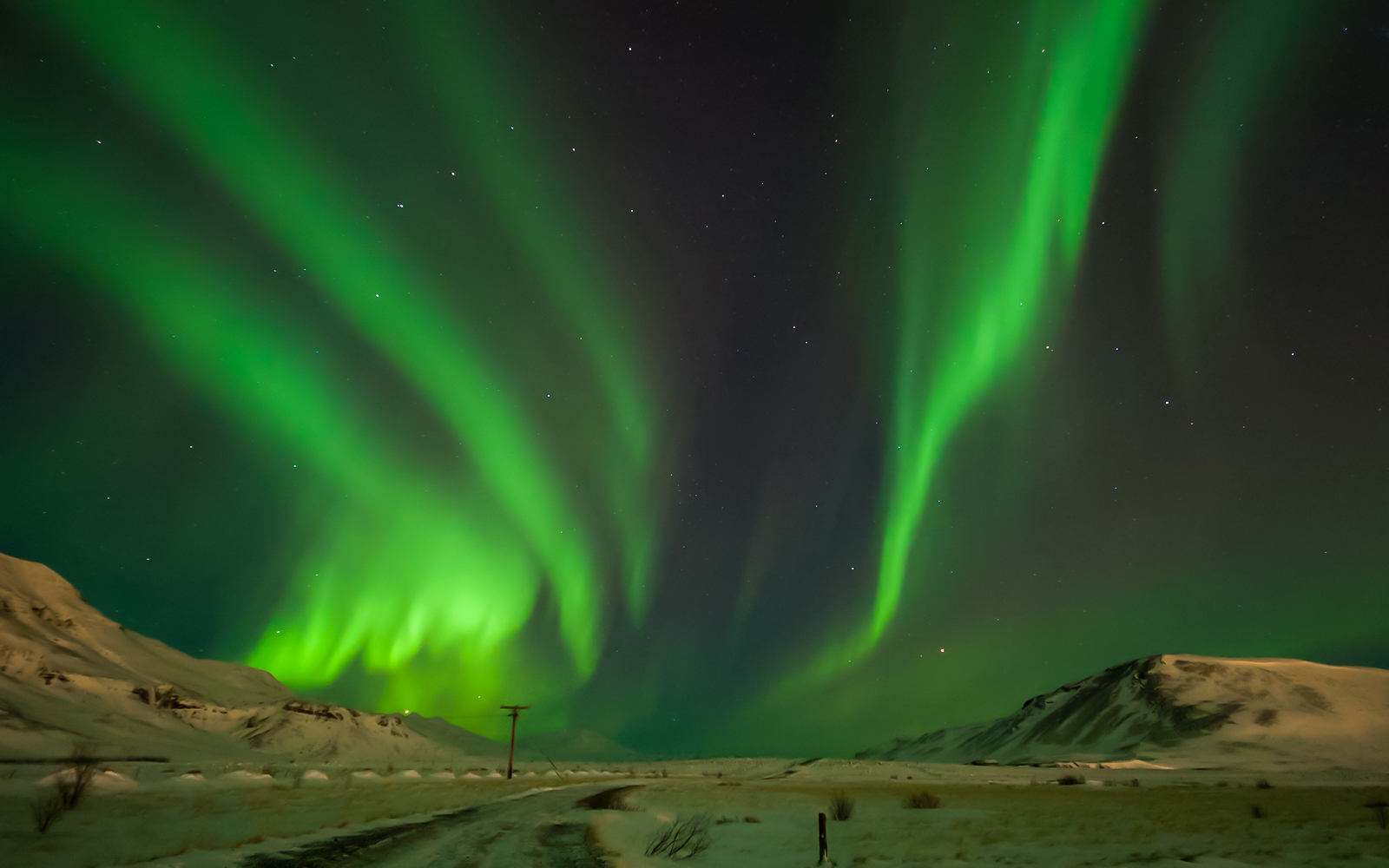 Northern lights over snowy landscape in Hvalfjörður, Iceland.