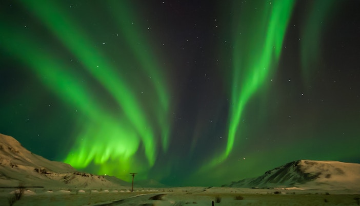 Northern lights over snowy landscape in Hvalfjörður, Iceland.