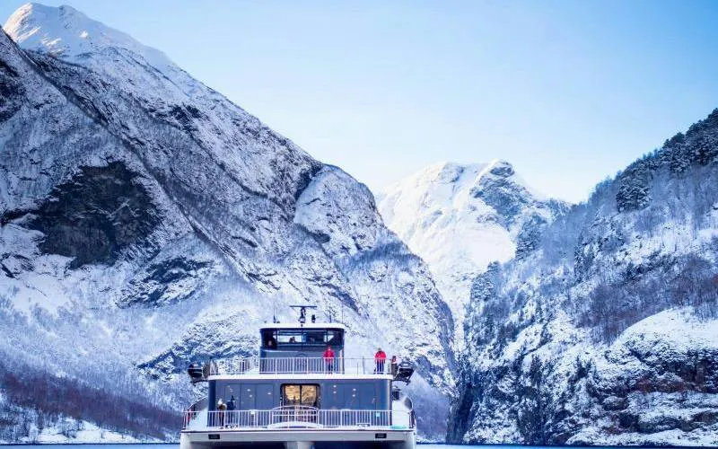 Cruise ship on Nærøyfjord with snow-covered mountains, part of Bergen to Flåm Railway tour.