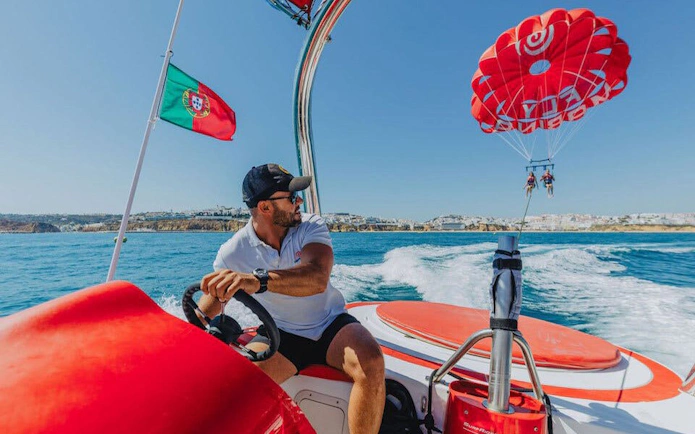 Parasailing adventure over the ocean in Albufeira, Portugal, with a boat and parasail in view.