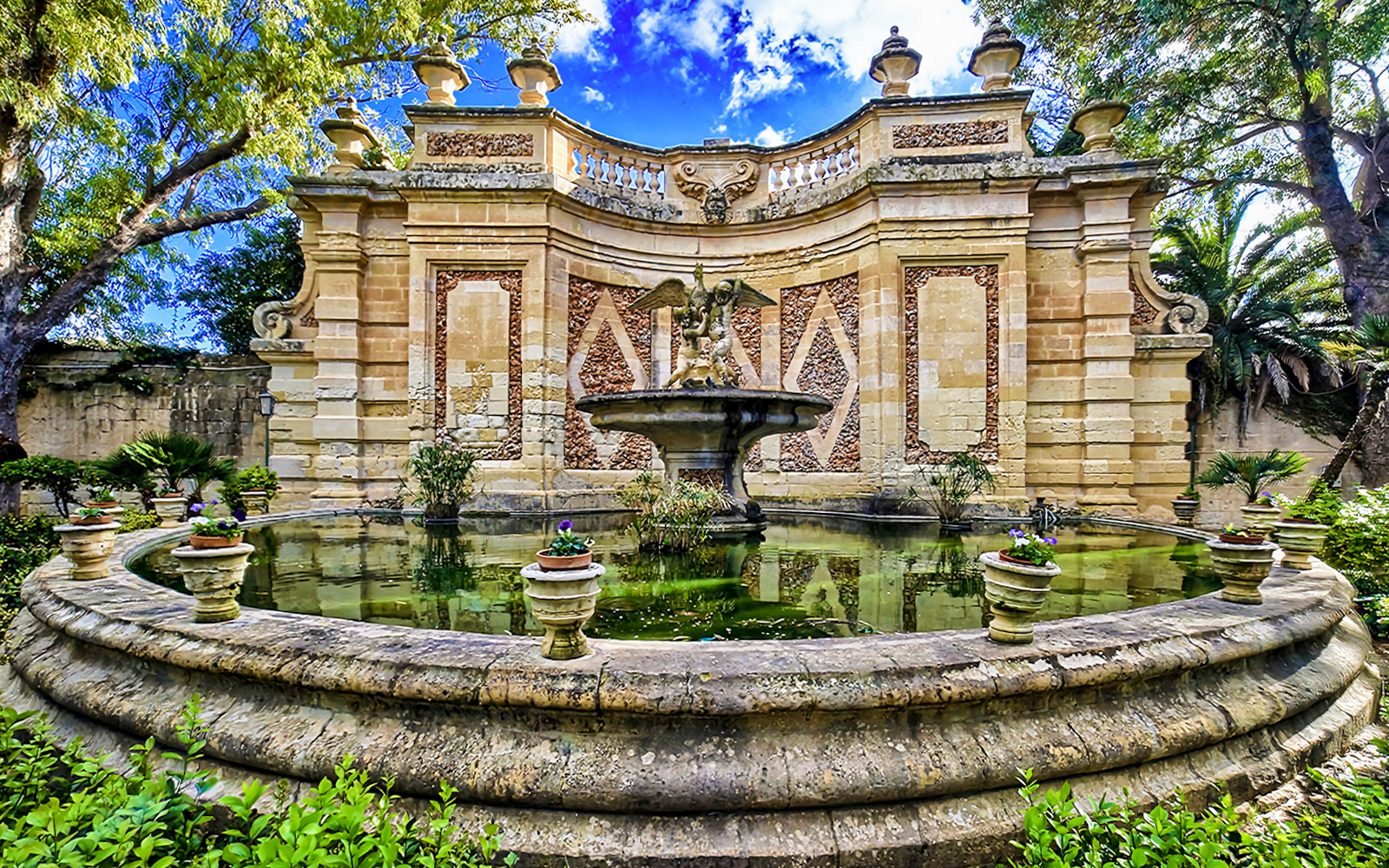 Fountain and ornate stone wall in a garden, Mdina, Malta.