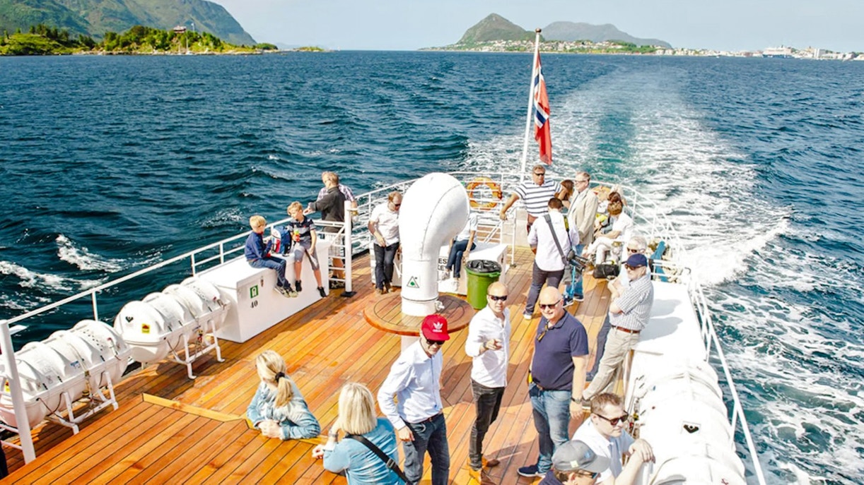 Sightseeing cruise passengers on deck, Hjørundfjord, Norway, with scenic mountain views.