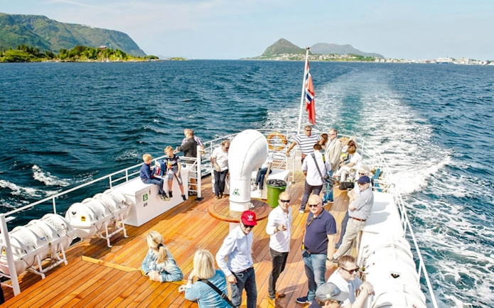 Sightseeing cruise passengers on deck, Hjørundfjord, Norway, with scenic mountain views.