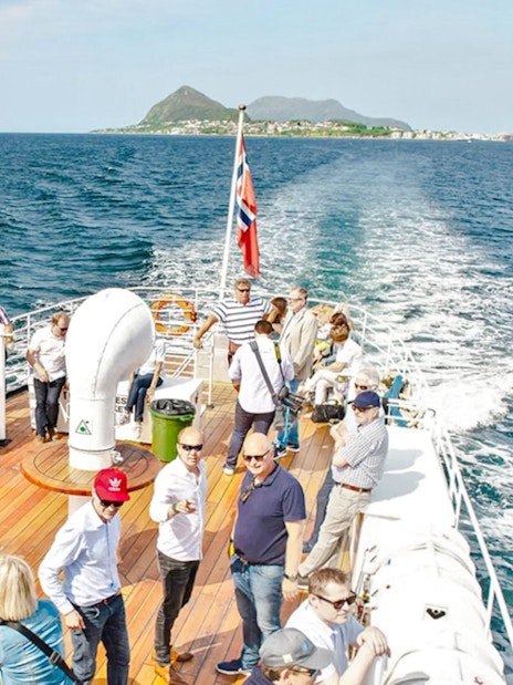 Sightseeing cruise passengers on deck, Hjørundfjord, Norway, with scenic mountain views.