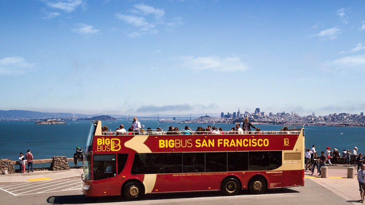 Turistas disfrutando del tour en autobús turístico de San Francisco, en un día soleado, con el emblemático puente Golden Gate de fondo.