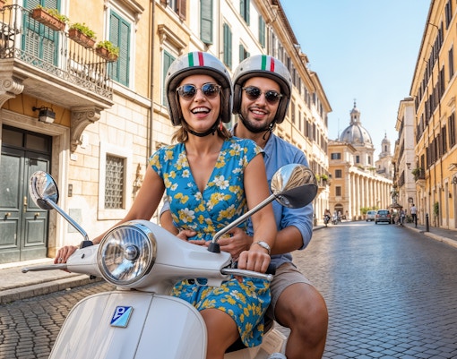 Couple riding a Vespa on a cobblestone street in central Rome with historic buildings.
