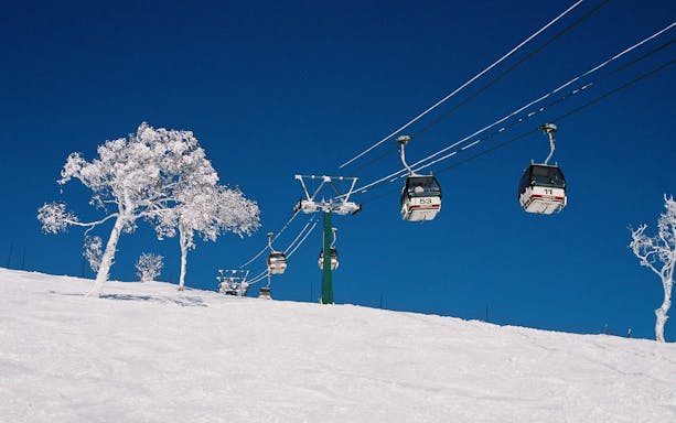 Ski lift with snowy trees in Rusutsu, Japan, under clear blue sky.