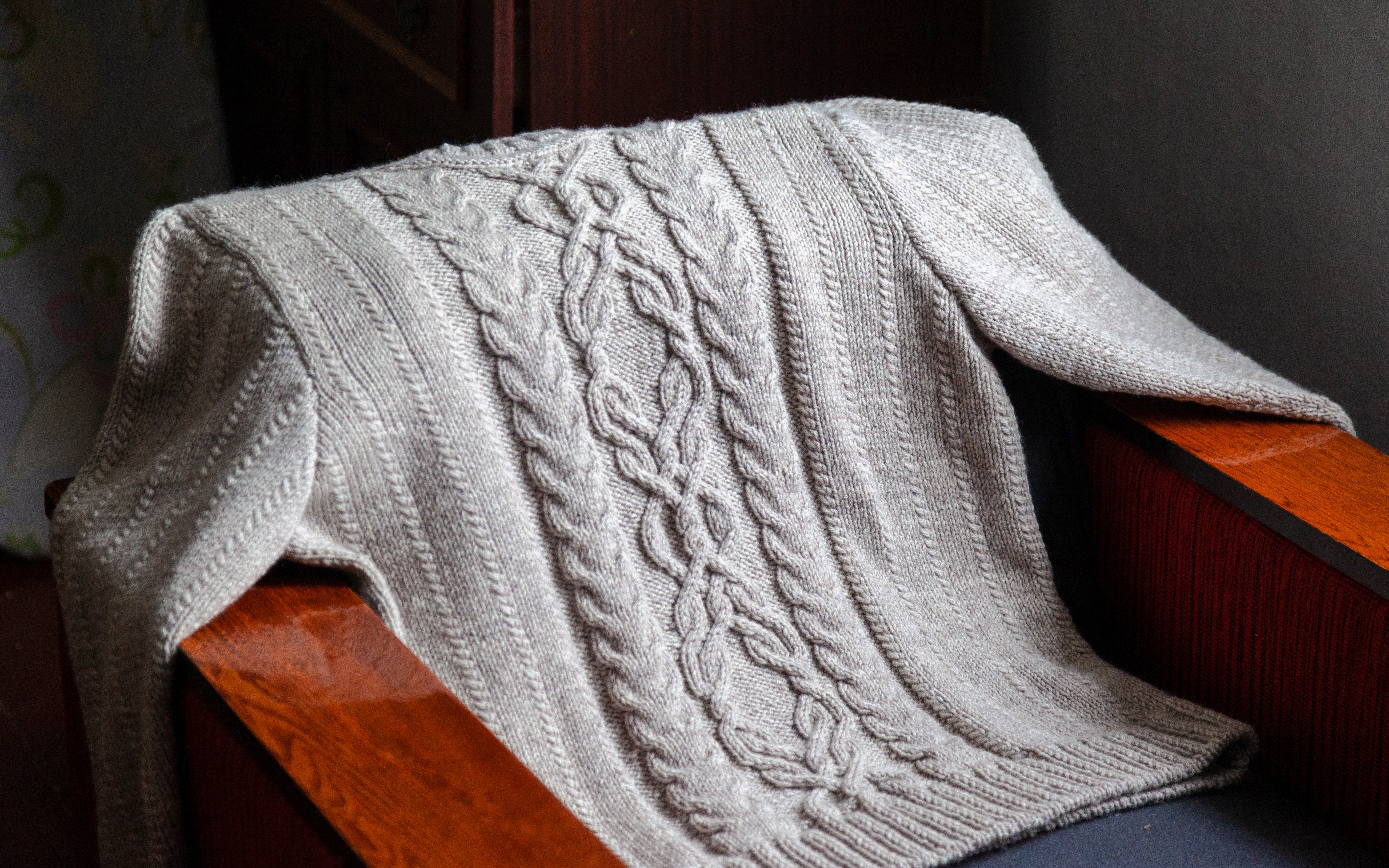 Aran sweater with cable knit pattern draped over a wooden chair in Ireland.