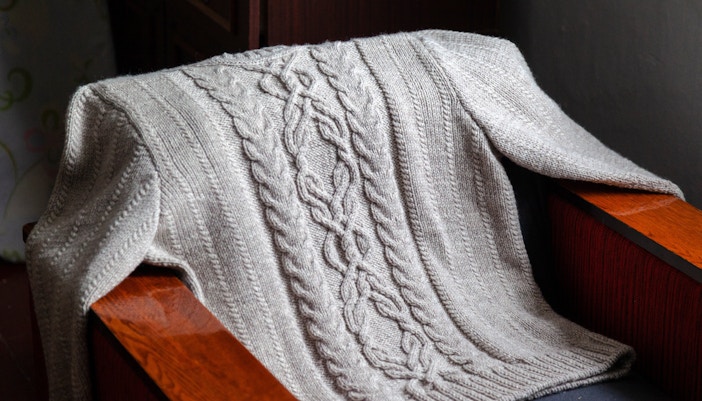 Aran sweater with cable knit pattern draped over a wooden chair in Ireland.