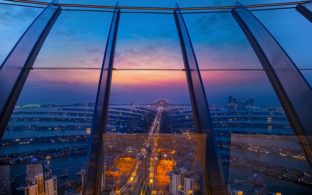 View from The Palm, Dubai at sunset, showcasing city lights and skyline.