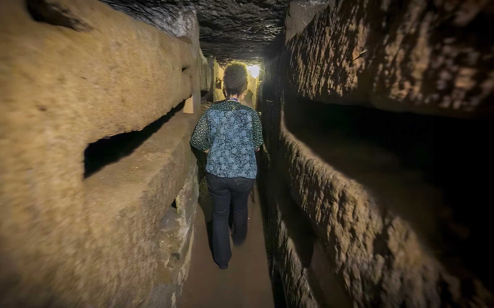 Person walking through narrow passage in Roman Catacombs during guided tour.