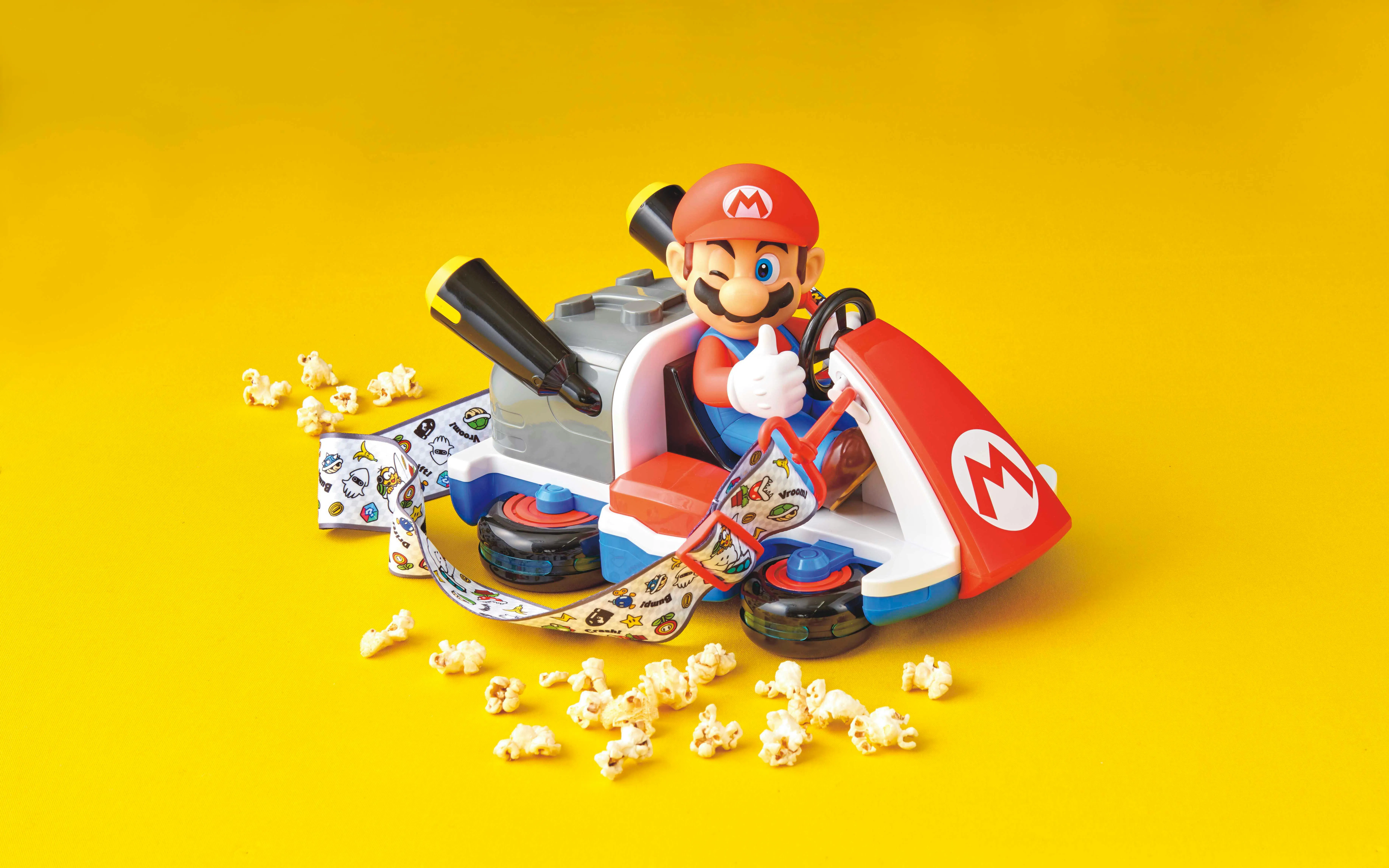Mario kart toy with themed strap surrounded by popcorn on yellow background at USJ.