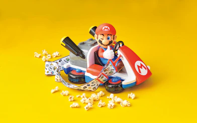 Mario kart toy with themed strap surrounded by popcorn on yellow background at USJ.