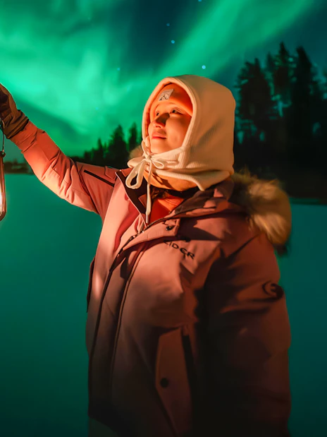 Guest holding lantern under Northern Lights on Rovaniemi bus tour.