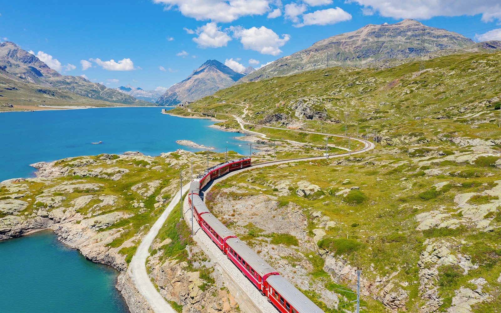 Bernina Pass train traveling beside a serene lake with mountain views in Switzerland.