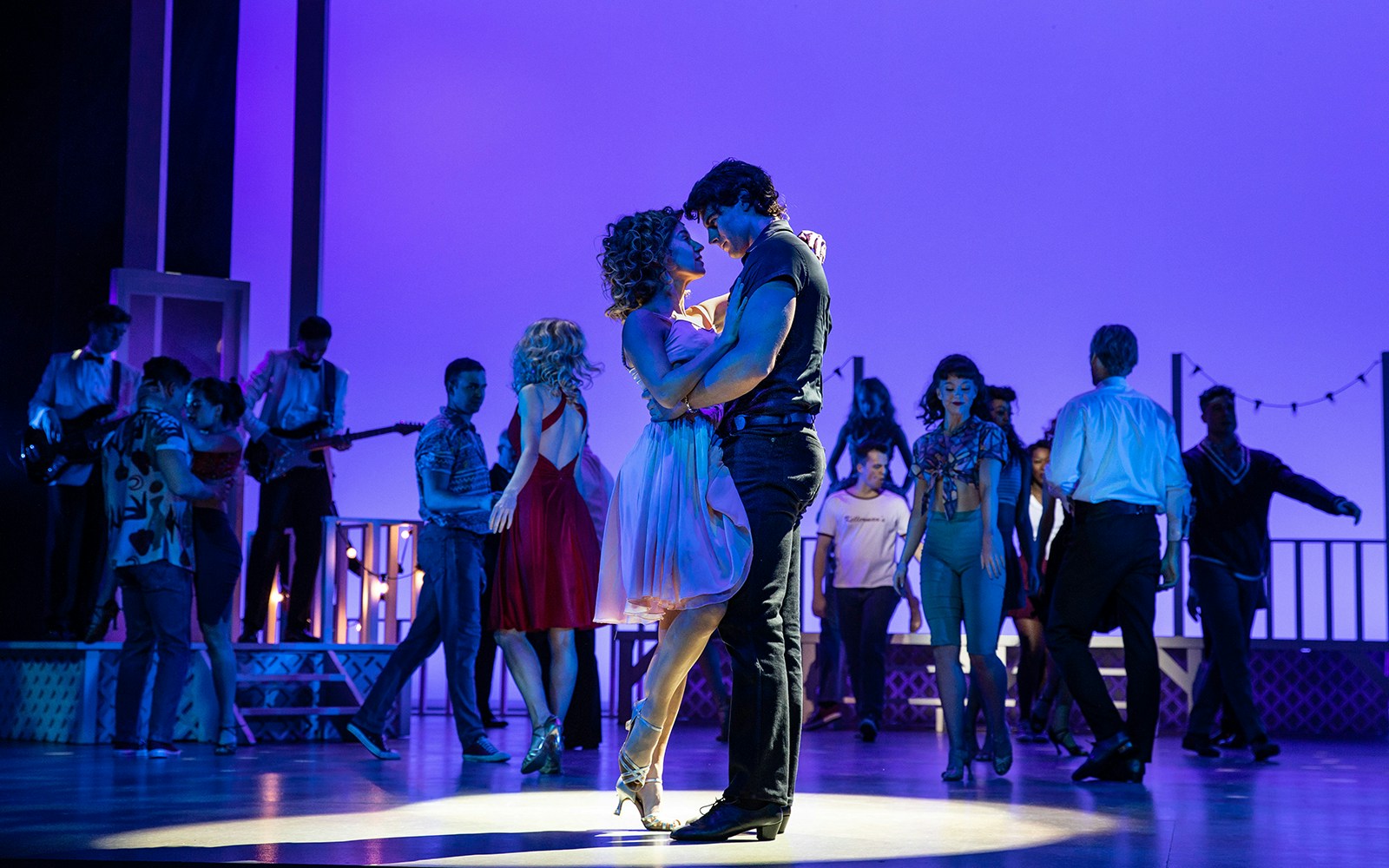 Couple dancing on stage during a "Dirty Dancing" performance with a live band in the background.