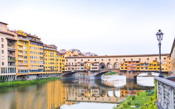Ponte Vecchio over the Arno River in Florence, Italy, viewed from a riverside path.