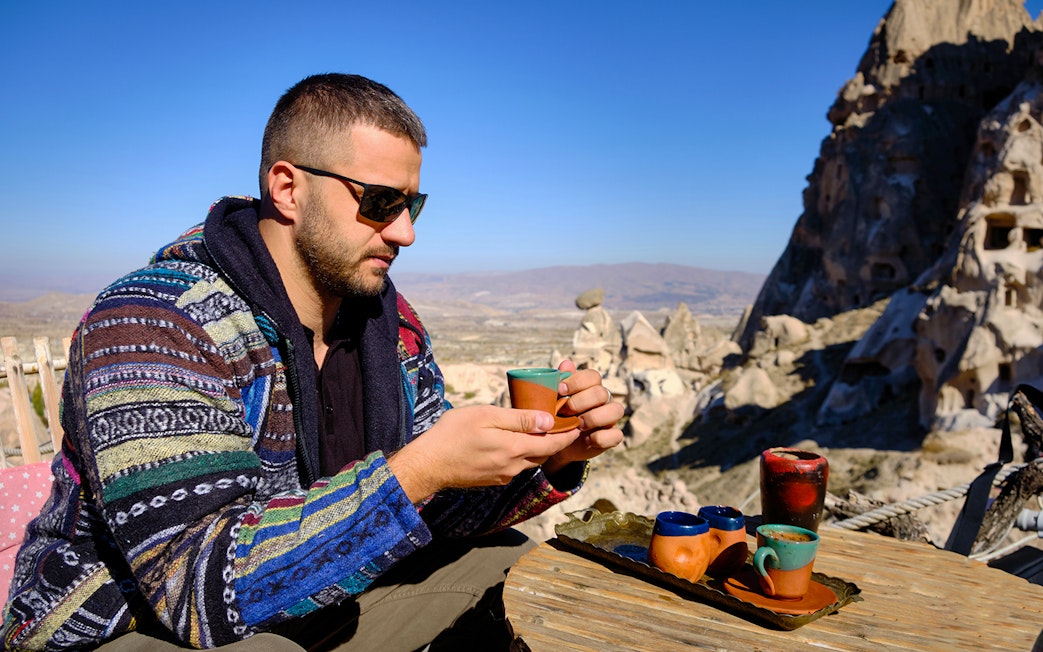 Guest savoring traditional drink at a local restaurant in Cappadocia with rock formations in view.