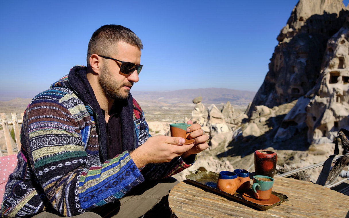 Guest savoring traditional drink at a local restaurant in Cappadocia with rock formations in view.