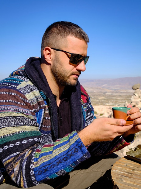Guest savoring traditional drink at a local restaurant in Cappadocia with rock formations in view.