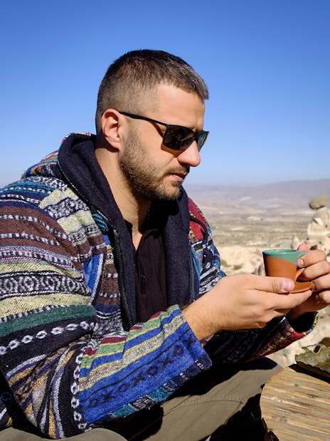Guest savoring traditional drink at a local restaurant in Cappadocia with rock formations in view.
